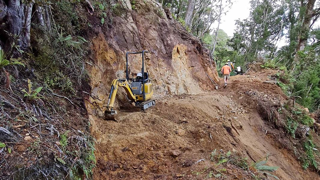 A small digger works on a muddy piece of track in a forest.