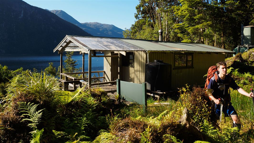 Small building by trees near water and hills. 