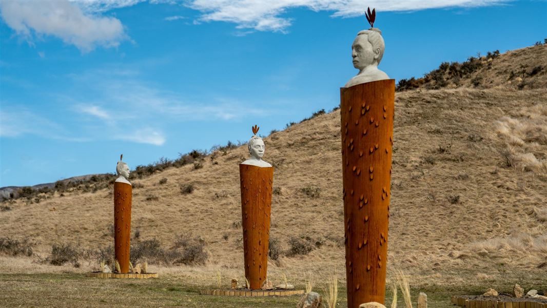 Three tall statues in white stone with large sculpted cloaks in a deep rust colour.