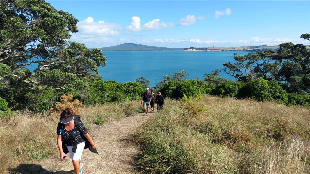 A group walking up a smooth track, heading to the top of a hill, with a view of the ocean behind them