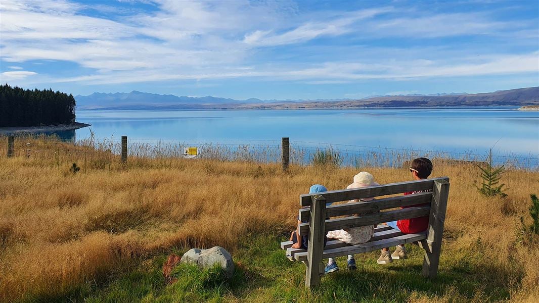 Three children on a seat looking over a calm lake.