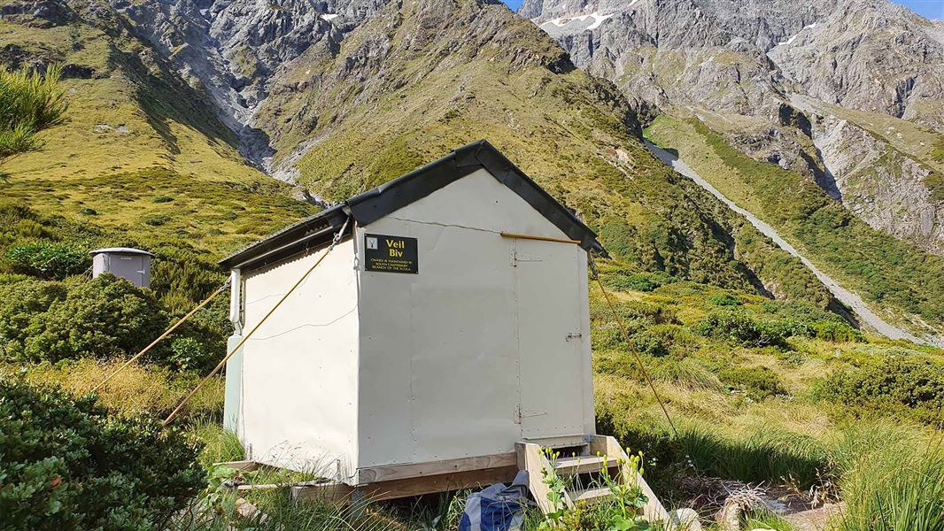 A small hut nestled at the base of several mountains.