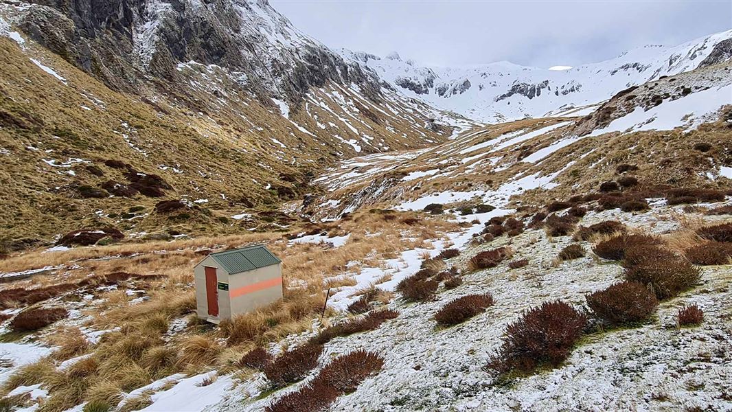 A small hut on an alpine plateau surrounded by snowy peaks.